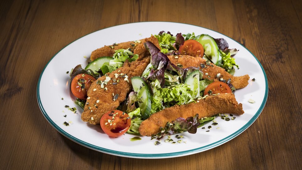 Salad with breaded fillets, tomatoes, and cucumbers on a plate. | © Glöckl Bräu