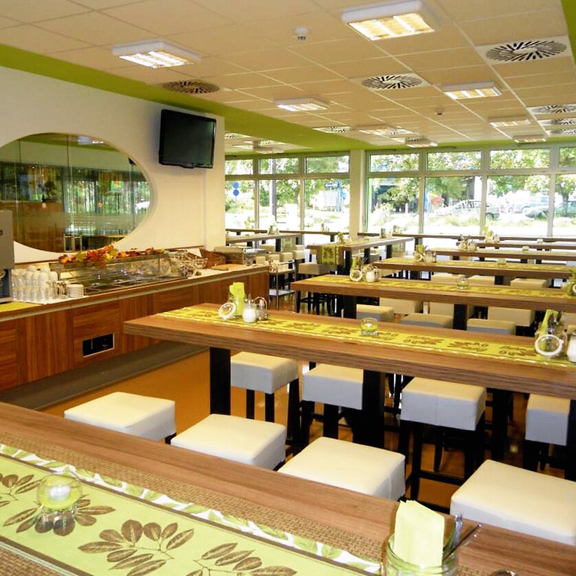 Modern dining area with long wooden tables and white chairs. | © Greenrooms