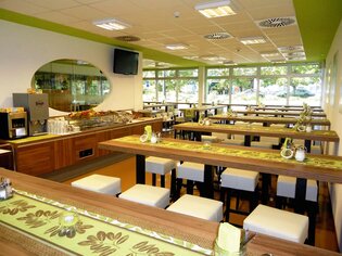 Modern dining area with long wooden tables and white chairs. | © Greenrooms