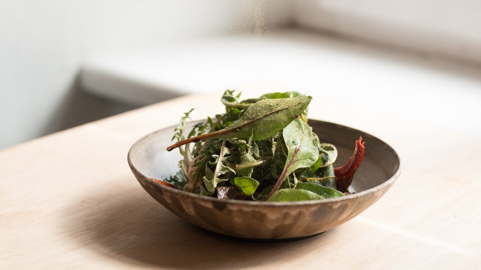 Una mano usa un setaccio per cospargere spezie su un'insalata. | © Kabuff