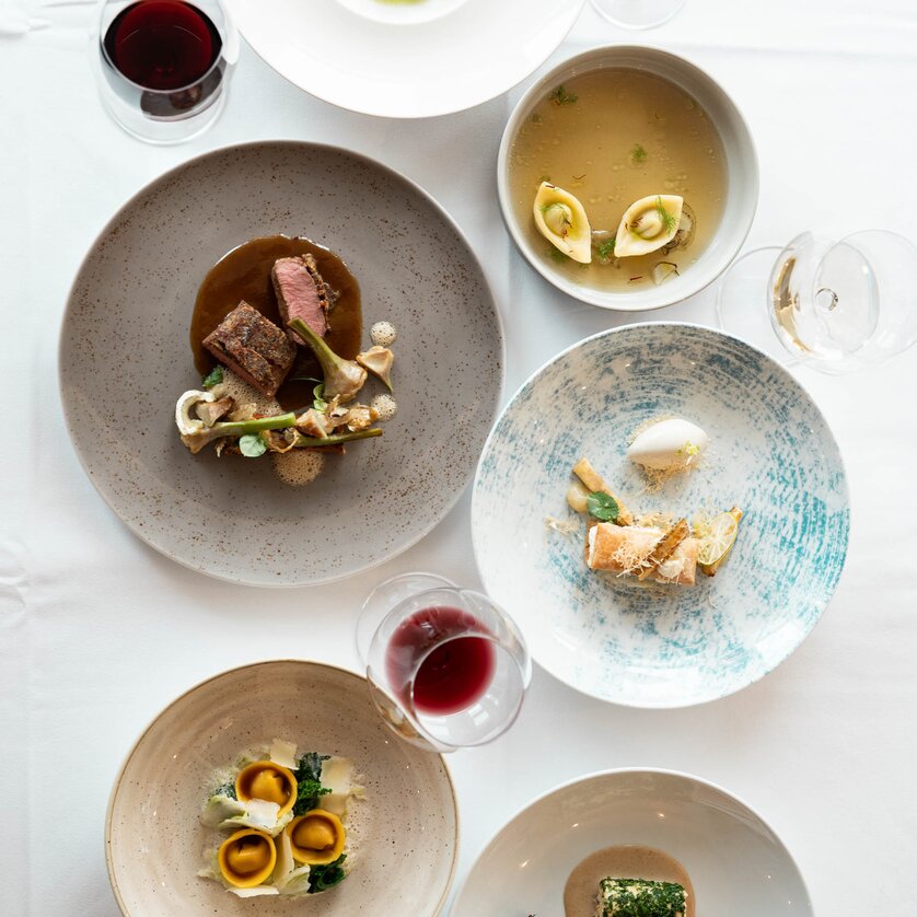 Verschiedene kunstvoll angerichtete Gerichte auf Tischen. | © Studio-Lou - Lukas Elsneg