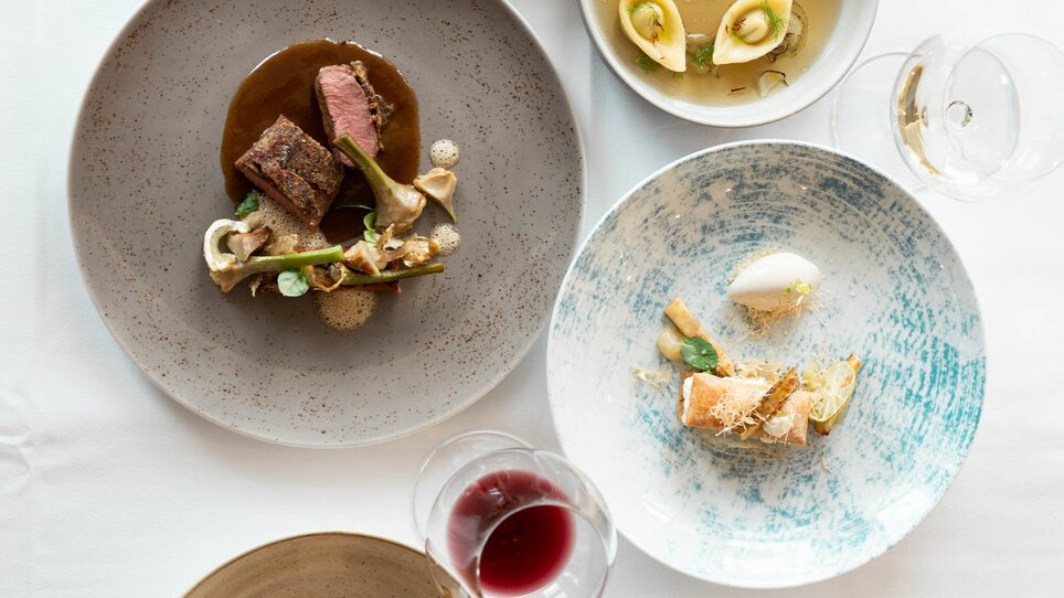 Verschiedene kunstvoll angerichtete Gerichte auf Tischen. | © Studio-Lou - Lukas Elsneg