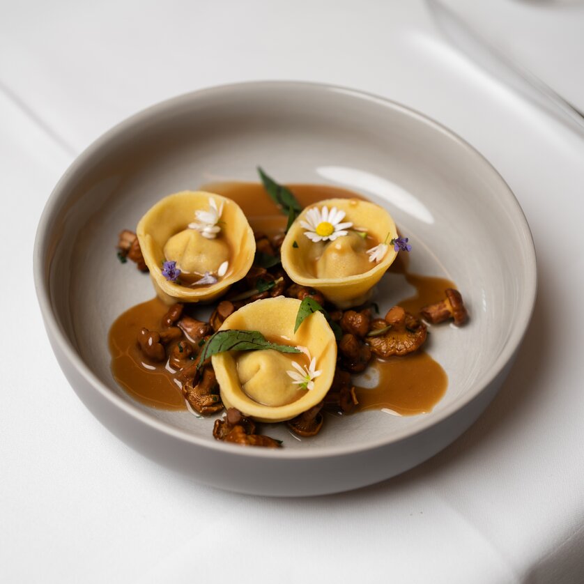 Ein Teller mit Ravioli, Kräutern und Blumen auf Soße. | © Lukas Elsneg