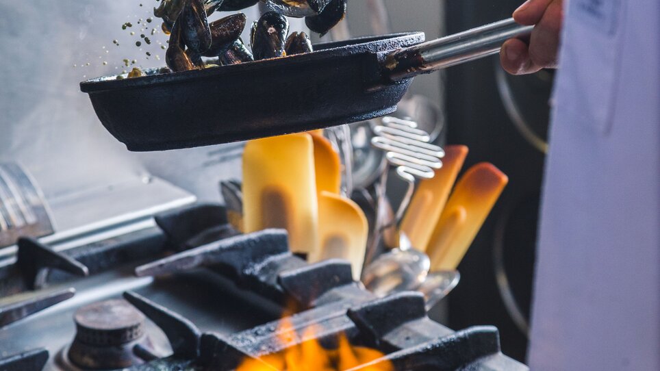 Chef cooking mussels over fire in a kitchen.