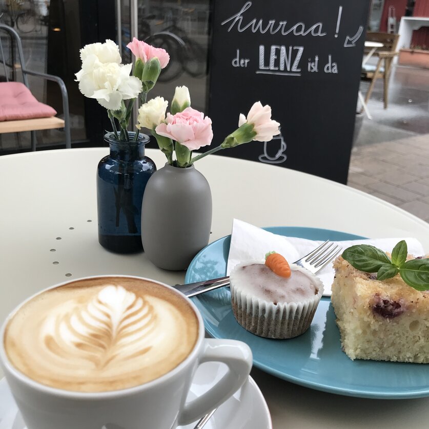 Ein Kaffee, Kuchen und frische Blumen in einem Café.