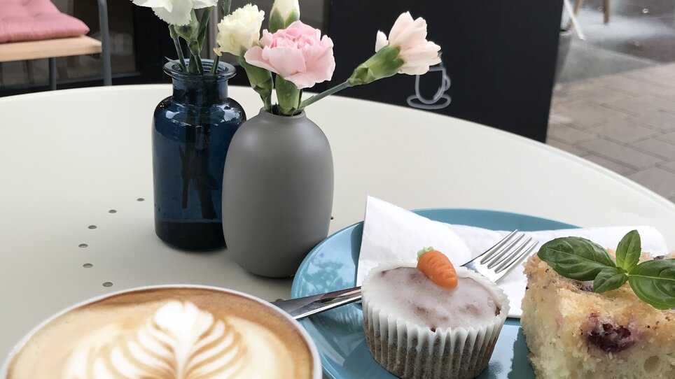 Ein Kaffee, Kuchen und frische Blumen in einem Café.