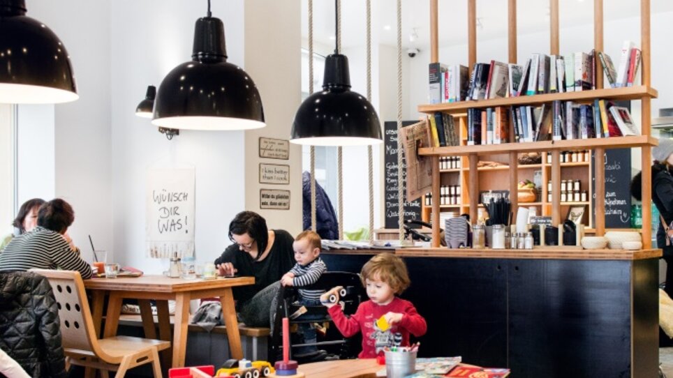Gemütliches Café mit Bücherregal, Tischen und spielenden Kindern. | © Martin Auer 