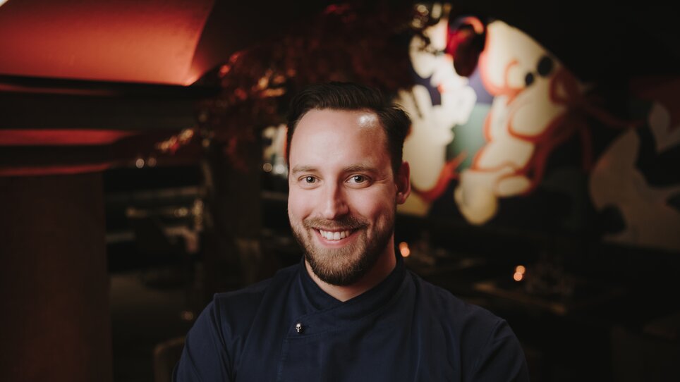 A smiling chef in a restaurant with modern decor.
