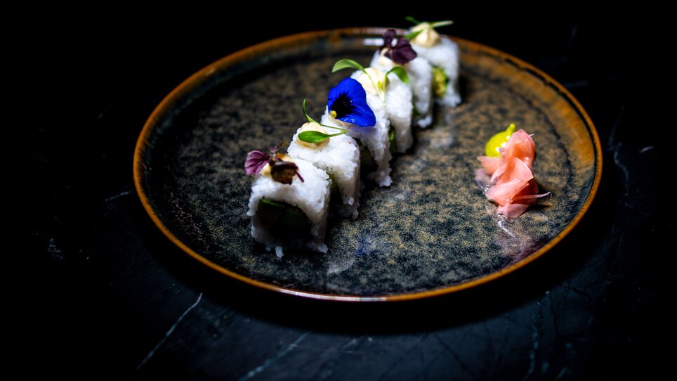 Artistic sushi with edible flowers and ginger on a black plate.