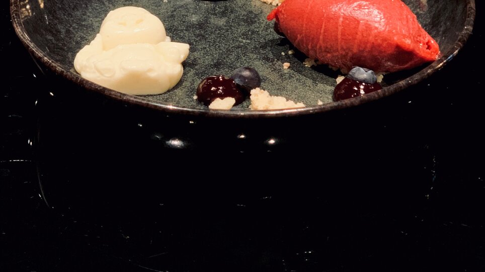 Creative dessert in a black bowl with sorbet and berries.