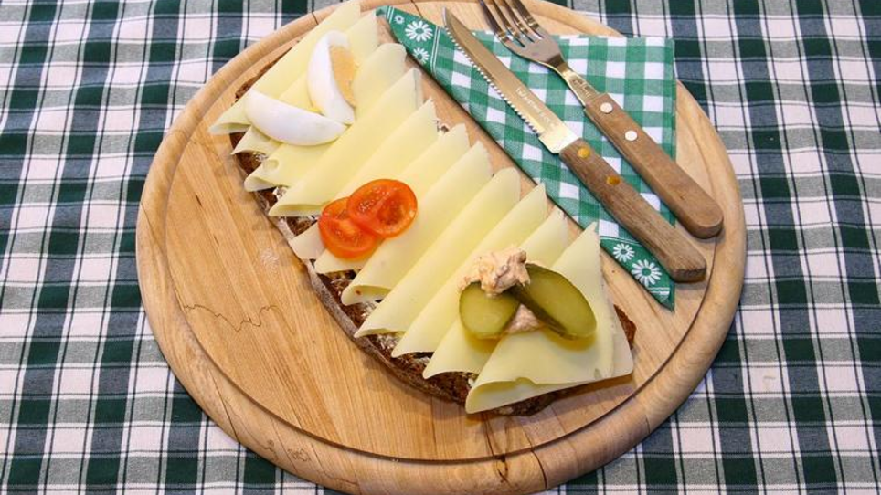 A wooden board with a cheese sandwich, garnished with gherkins, egg and tomatoes. | © Murheuriger
