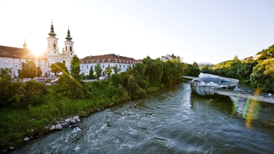 Die Murinsel in Graz mit dem Fluss Mur und der Aussicht auf die Stadt. | © Steiermark Tourismus - ikarus
