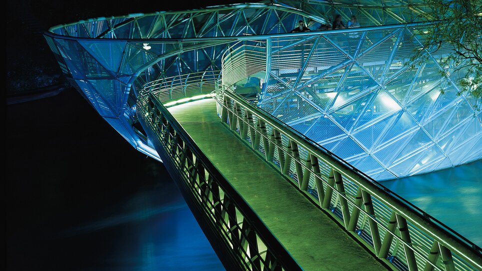 Die Murinsel bei Nacht mit beleuchtetem Steg im Wasser. | © Graz Tourismus - Harry Schiffer