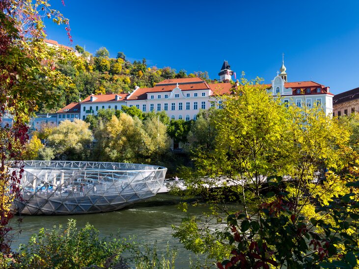 Die Murinsel in Graz mit Blick auf den Fluss Mur und die umliegenden Bäume. | © Graz Tourismus - Harry Schiffer