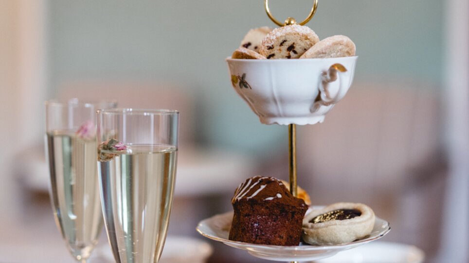 Elegantes Etagere mit einer Auswahl an feinem Gebäck und zwei Gläsern Sekt. | © Omas Teekanne