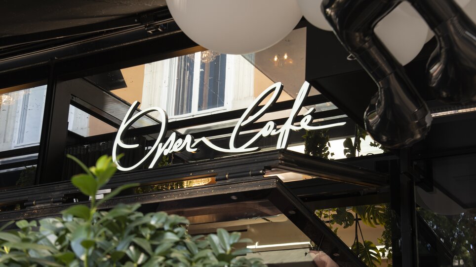 Illuminated sign of the Operncafé with plants in the foreground. | © Jauk Katharina