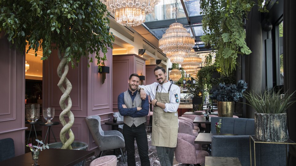 Two men at the Operncafé, elegantly decorated room with plants and chandeliers. | © Jauk Katharina