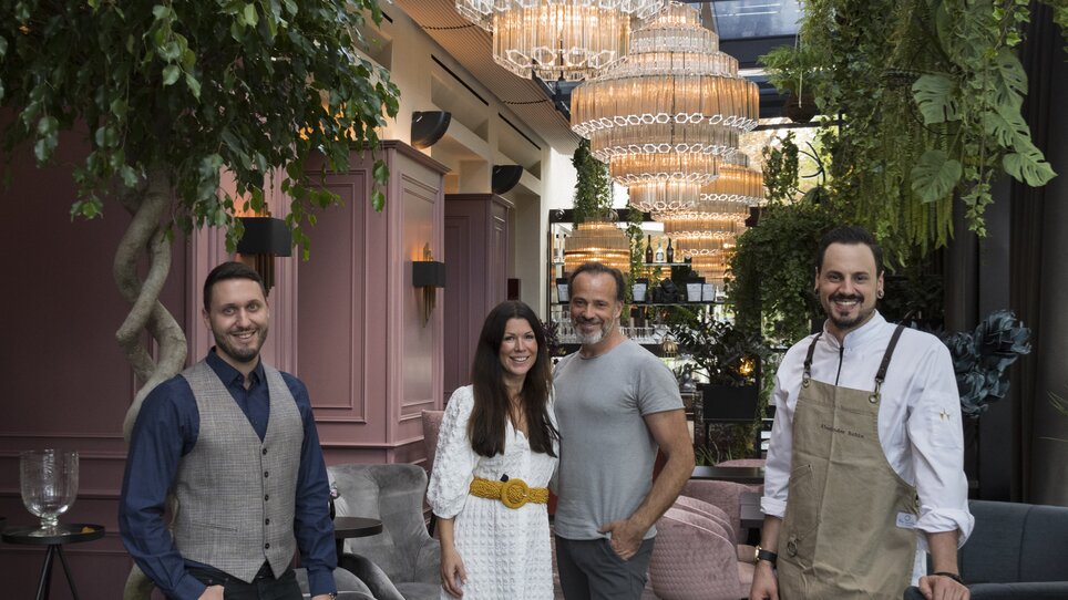 Four people pose in a stylish restaurant with large chandeliers. | © Jauk Katharina