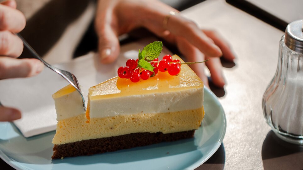 A slice of cheesecake with fruit and a fork on a plate in a café. | © Bobbys Agency