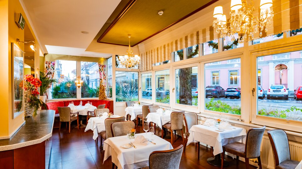 Elegant restaurant with garden view, white tables, cozy atmosphere. | © Parkhotel