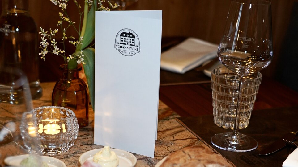 Table with menu, bread, cold cuts, and flowers in a restaurant. | © Wirtshaus Schanzlwirt
