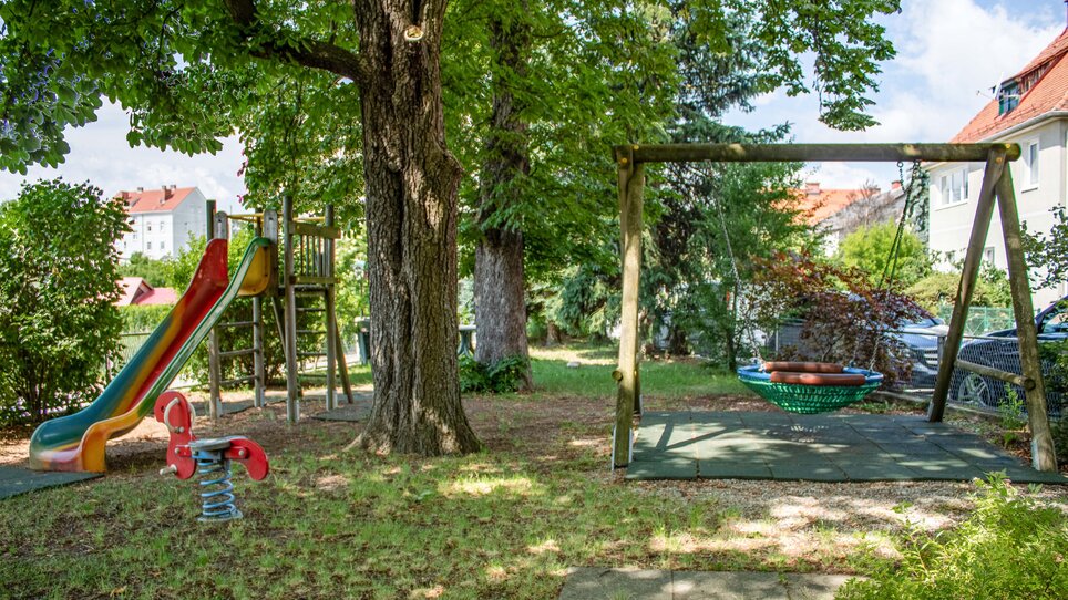 Spielplatz mit Rutsche, Schaukel und Wippe in einer grünen Umgebung. | © sReindl