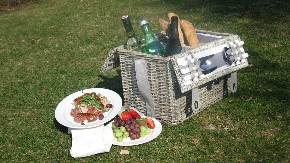 A picnic basket on a lawn with food and drinks. | © Starcke Haus
