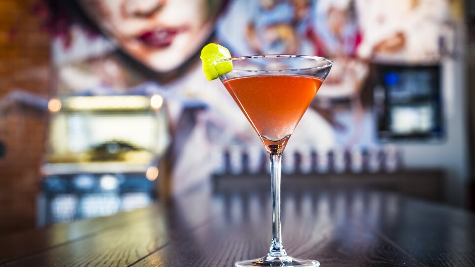Un elegante cocktail in un bicchiere, guarnito con una fetta di lime, su uno sfondo di murales.