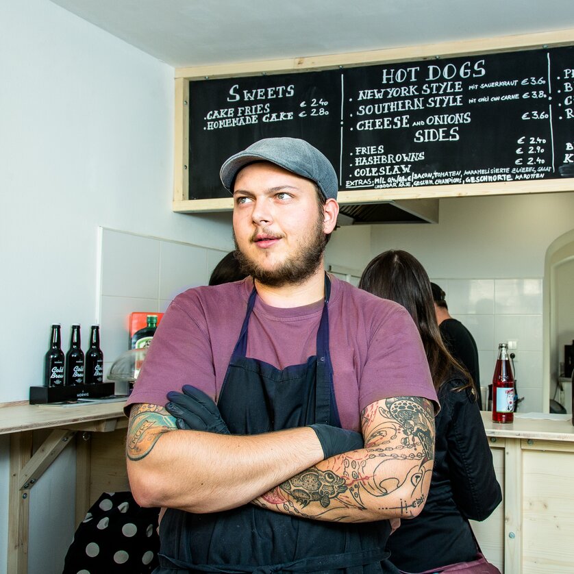 Man behind the counter of a restaurant with a menu above. | © The Hungry Heart