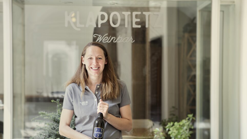 Frau hält Weinflasche vor der Klapotetz Weinbar in Graz. | © Klapotetz