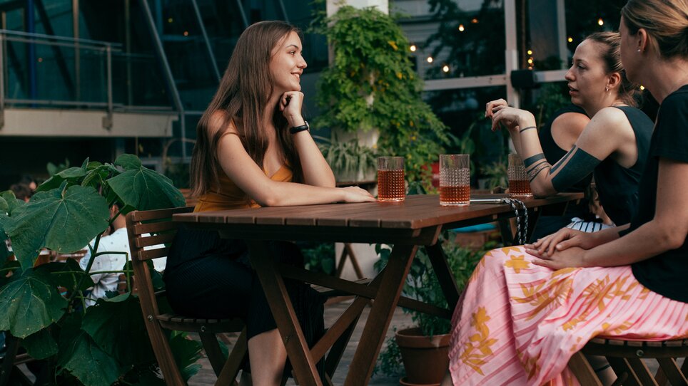 Three women engage in conversation at a garden café in Graz. | © Graz Tourismus