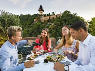 Friends enjoying dinner with a view of the Graz Clock Tower and the city. | © Graz Tourismus - Werner Krug
