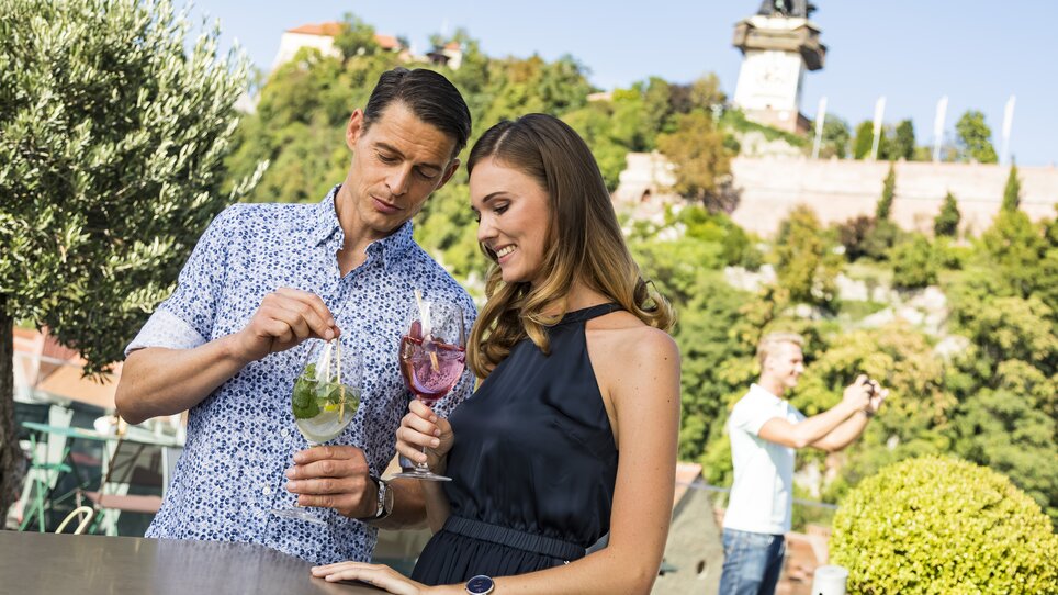 Paar genießt Cocktails in der GenussHauptstadt Graz mit Uhrturm im Hintergrund. | © Graz Tourismus - Werner Krug