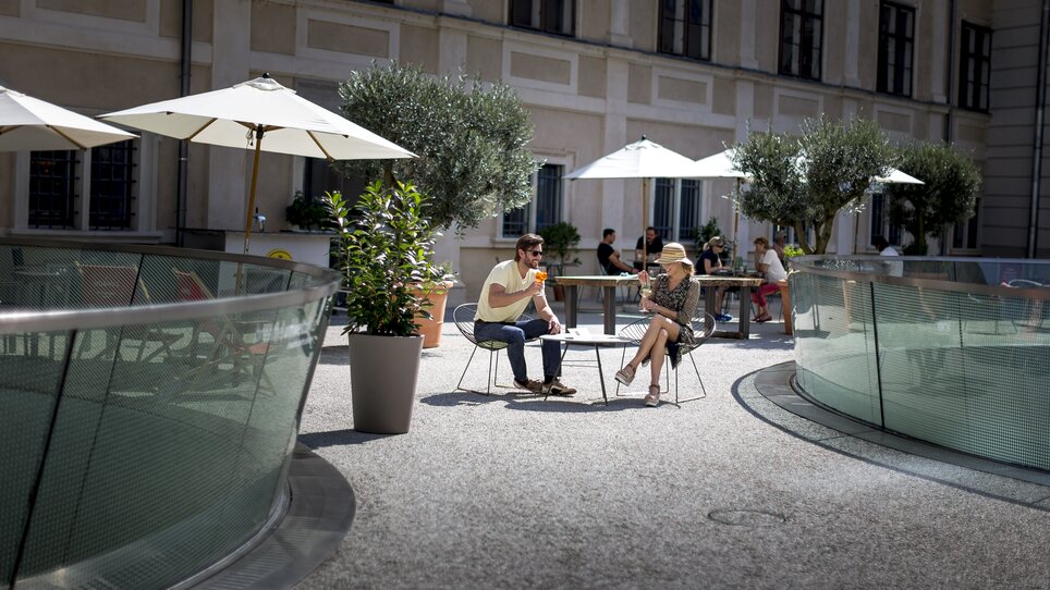 Paar genießt drinks im Freien in Graz, umgeben von Bäumen und Sonnenschirmen. | © Graz Tourismus - Tom Lamm