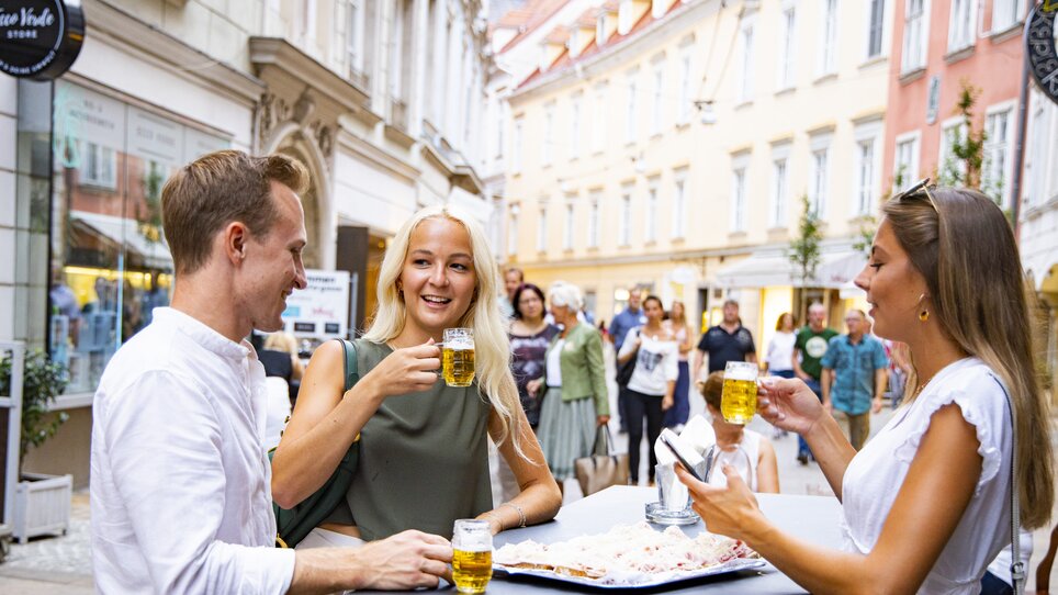 Freunde genießen Bier und lokale Speisen im Freien in Graz. | © Graz Tourismus - Werner Krug