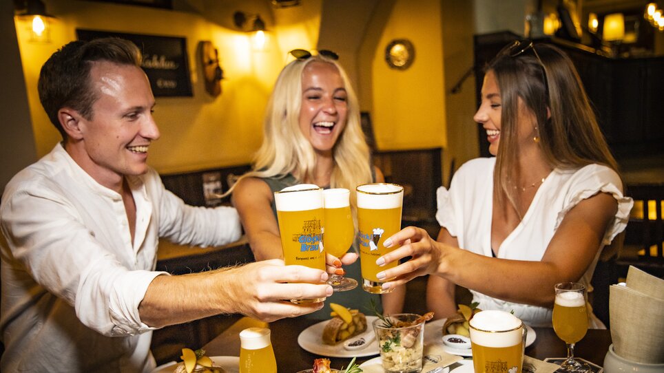 Freunde stoßen mit Bier an und genießen Essen in Graz. | © Graz Tourismus - Werner Krug
