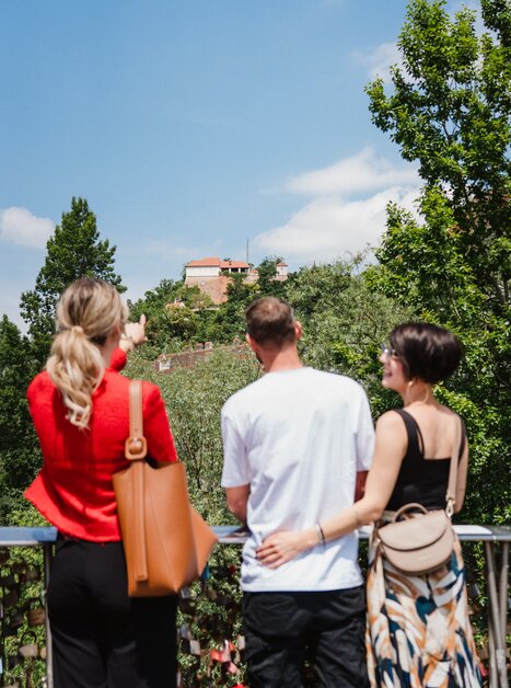 Drei Personen blicken auf den Grazer Schlossberg - bei einem geführten Stadtrundgang. | © 5komma5sinne - MotionAds