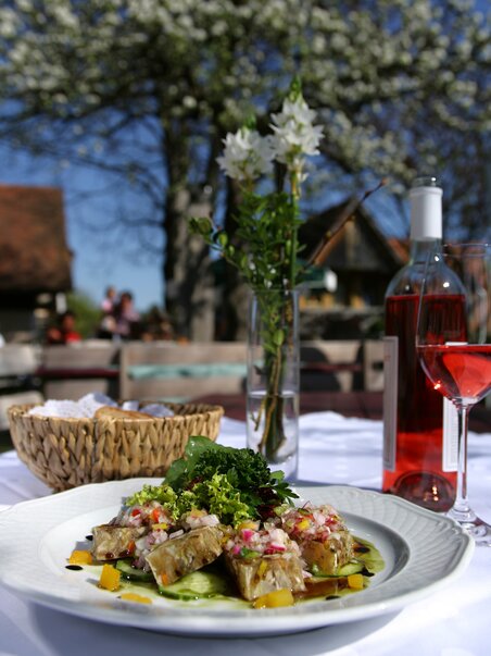A plate of fish and vegetable dish, rosé wine in the background. | © Graz Tourismus - Harry Schiffer
