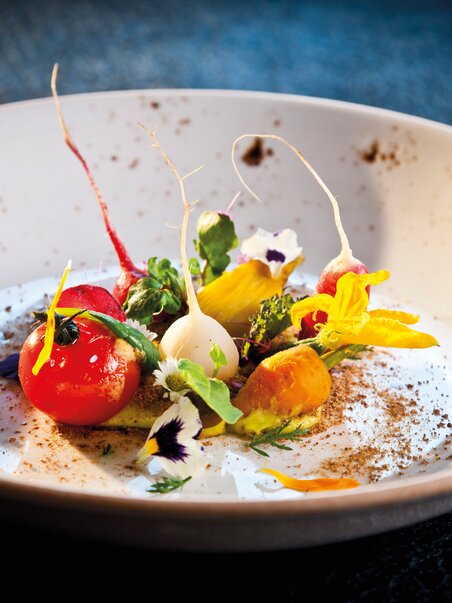 Ein kunstvoll angerichtetes Gourmetgericht mit bunten Zutaten und Blüten. | © Graz Tourismus - Werner Krug
