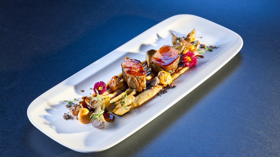 Elegant dish with meat, vegetables, and sauce on a long plate. | © Werner Krug