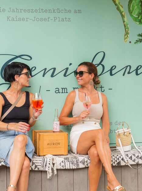 Two women enjoy drinks in Graz in front of a wall with writings. | © 5komma5sinne - Helmut Schweighofer
