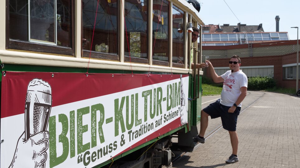 L'uomo posa accanto al tram della cultura della birra con un grande striscione. | © Tramway Museum Graz
