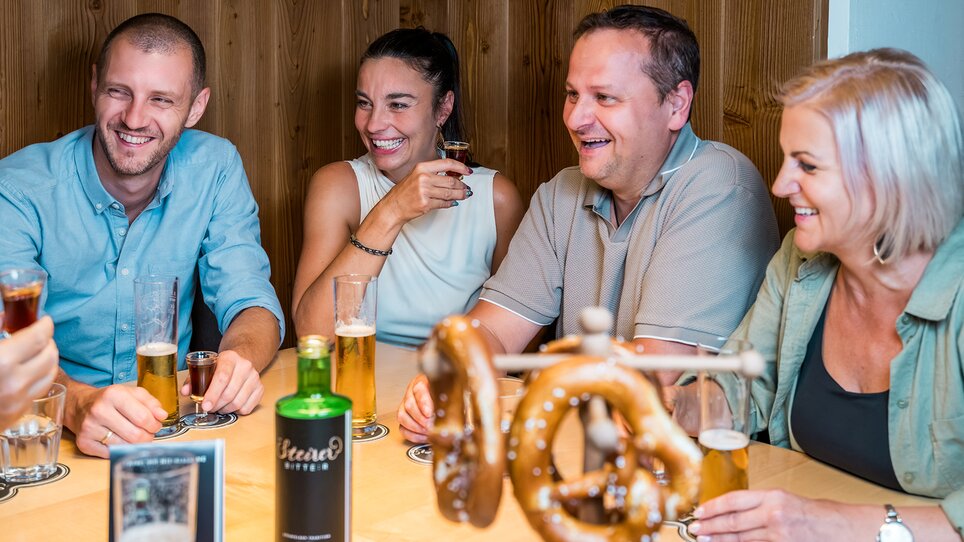 Quattro persone si divertono a un incontro sociale con birra e pretzel. | © Mias Photoart