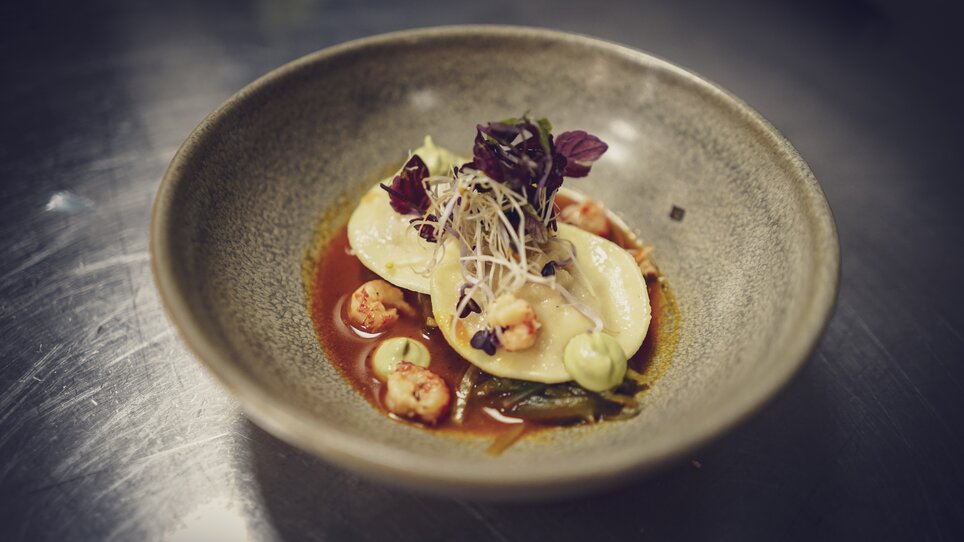 Un piatto artisticamente impiattato con ravioli, gamberetti e salsa verde. | © ROLLING PIN