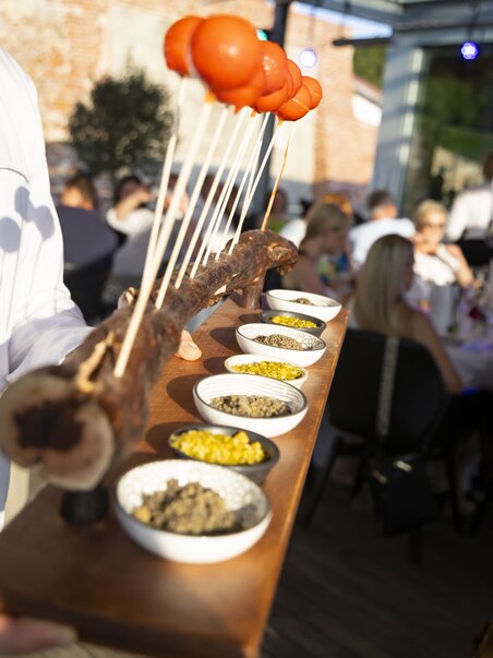 A waiter serves a wooden platter with various dips and colorful snacks. | © Graztourismus - Werner Krug