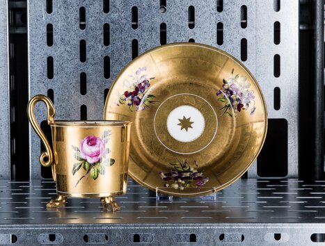 Ein goldener Becher und Untertasse mit Blumenmotiven auf einem Regal. | © Markus Mansi_MOMA