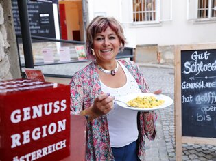 Frau lächelt mit einem Teller Essen vor einem Geschäft in Graz. | © UMJ - Lackner