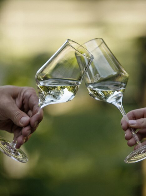 Two wine glasses with white wine clink together. | © Hubert Uranjek