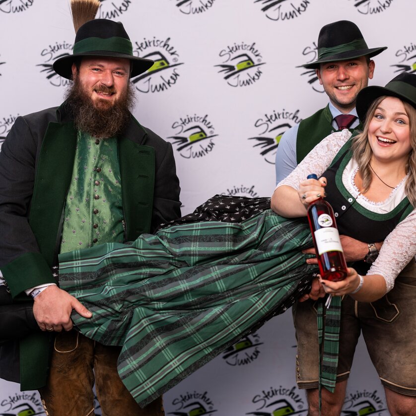 Steirische Junkerpräsentation I Graz | © Wein Steiermark - Fotokuchl Eine fröhliche Gruppe in Tracht präsentiert eine Flasche Wein auf einer Veranstaltung. | © Wein Steiermark - Fotokuchl