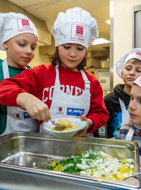 Vier Kinder in Kochmützen bereiten gemeinsam ein Gericht vor. | © Graz Tourismus - Paul Stajan